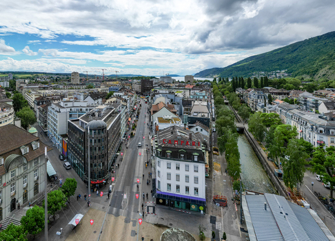 Aerial view of urban cityscape with a central street historic buildings and a canal running alongside lush green trees under a cloudy sky in Biel Bienne Canton of Bern Switzerland. Aerial view of urban cityscape with a central street historic buildings and a canal running alongside lush green trees under a cloudy sky in Biel Bienne Canton of Bern Switzerland.