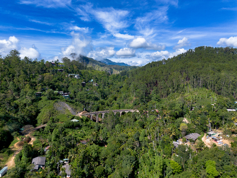 Aerial view of the historic Nine Arch Bridge nestled within dense green jungle and rolling hills under a clear blue sky in Demodara Uva Province Sri Lanka. Aerial view of the historic Nine Arch Bridge nestled within dense green jungle and rolling hills under a clear blue sky in Demodara Uva Province Sri Lanka.