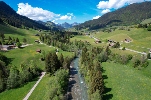 Aerial view of a lush green valley with a river flowing through scattered chalets and forested hills in Rougemont Vaud Switzerland. Aerial view of a lush green valley with a river flowing through scattered chalets and forested hills in Rougemont Vaud Switzerland.
