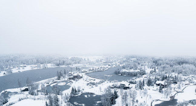 Aerial view of a snow covered landscape featuring frozen lakes dense pine forests and scattered wooden houses under a cloudy winter sky Latvia. Aerial view of a snow covered landscape featuring frozen lakes dense pine forests and scattered wooden houses under a cloudy winter sky Latvia.