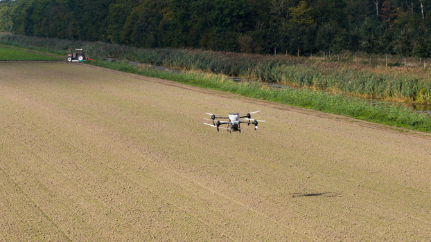 Aerial view of an agricultural drone spraying a field with a tractor visible in the background near a canal and trees in Zeewolde Flevoland Netherlands. Aerial view of an agricultural drone spraying a field with a tractor visible in the background near a canal and trees in Zeewolde Flevoland Netherlands.