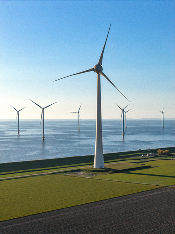 Aerial view of wind turbines standing in green fields and offshore in the sea under a clear blue sky Netherlands.