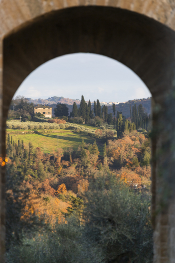 View of the rolling hills of the Tuscan countryside with a stone villa and cypress trees framed by a stone archway in Monteriggioni Tuscany Italy. View of the rolling hills of the Tuscan countryside with a stone villa and cypress trees framed by a stone archway in Monteriggioni Tuscany Italy.