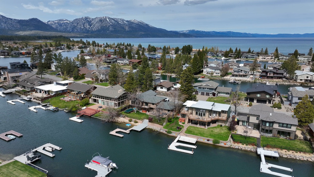 Aerial view of waterfront residential homes with private docks along the canal surrounded by pine trees and mountains in South Lake Tahoe California United States.