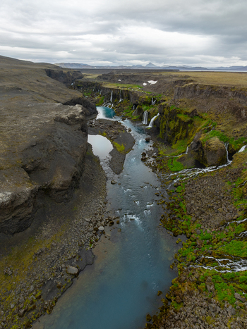 Aerial view of Sigoldugljufur canyon with turquoise glacial river cascading waterfalls mossy cliffs and rocky terrain under a cloudy sky in Rangarthing ytra Iceland. Aerial view of Sigoldugljufur canyon with turquoise glacial river cascading waterfalls mossy cliffs and rocky terrain under a cloudy sky in Rangarthing ytra Iceland.