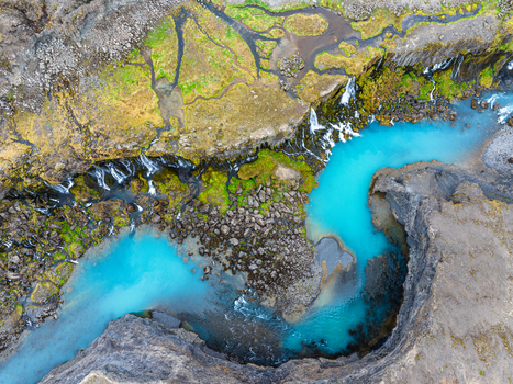 Aerial view of the winding Fjadrargljufur canyon with its vibrant turquoise glacial river flowing through steep rocky cliffs and mossy green terrain in Iceland. Aerial view of the winding Fjadrargljufur canyon with its vibrant turquoise glacial river flowing through steep rocky cliffs and mossy green terrain in Iceland.