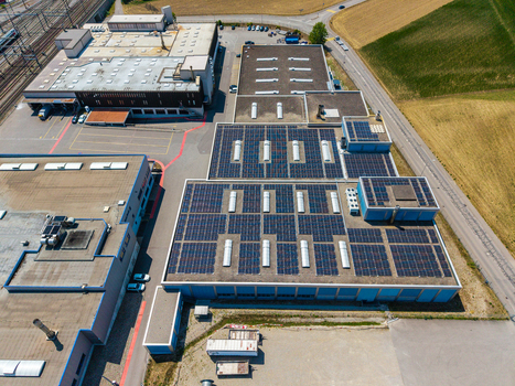 Aerial view of the Daniken storage area featuring large industrial buildings with extensive solar panel arrays on the rooftops surrounded by roads and fields in Daniken Solothurn Switzerland.