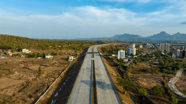 Aerial view of the JNPT highway stretching through the landscape near Badlapur with surrounding buildings hills and clear blue sky in Badlapur Maharashtra India. Aerial view of the JNPT highway stretching through the landscape near Badlapur with surrounding buildings hills and clear blue sky in Badlapur Maharashtra India.