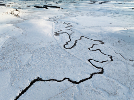Aerial view of a dark river snaking through a snow laden landscape a stark contrast of black against the pristine white Nasbinals Occitanie France.