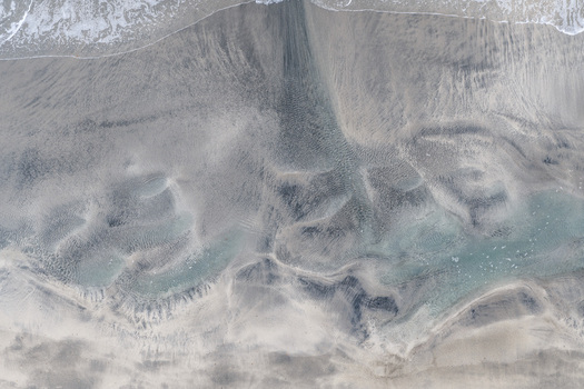 Aerial view of the sandy coastline of Senja featuring intricate patterns in the sand and clear shallow water along the shore in Senja Troms Norway.