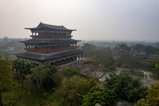 Aerial view of the World Peace Pagoda surrounded by lush trees and misty fields in Nepal.