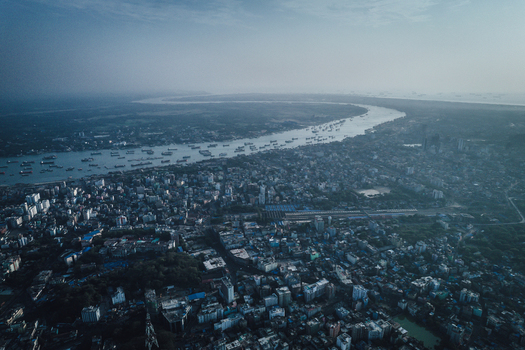 Chattogram Bangladesh 25 February 2022 Aerial view of the city of Chattogram featuring the Karnaphuli River with numerous ships and boats dense urban buildings and a hazy sky.
