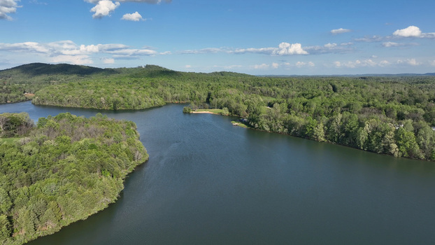 Aerial view of Mill Creek Lake surrounded by lush green forests under a bright blue sky with scattered clouds in Amherst County Virginia United States.