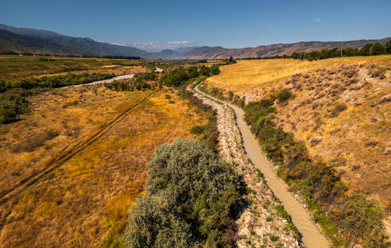 Aerial view of the Chon Kemin river winding through the golden dry landscape of the valley with distant mountains under a clear blue sky in Kemin Chuy Province Kyrgyzstan.