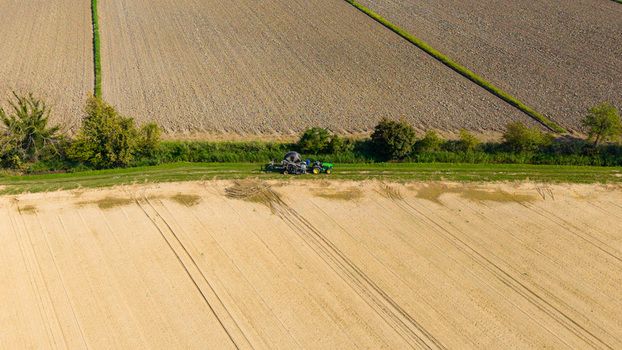 Aerial view of a tractor pulling a reel irrigation system across a cultivated agricultural field with tire tracks and green hedgerows in Milan Lombardy Italy. Aerial view of a tractor pulling a reel irrigation system across a cultivated agricultural field with tire tracks and green hedgerows in Milan Lombardy Italy.
