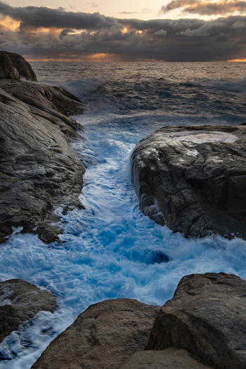 View of Torndirrup National Park with crashing waves rushing between dark rocky cliffs under a dramatic sunset sky Torndirrup Western Australia Australia.