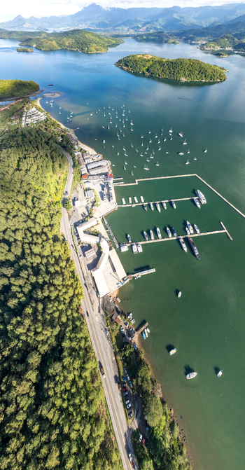Aerial view of the marina in Angra dos Reis with numerous boats docked in the bay surrounded by lush green hills and a coastal road Angra dos Reis Rio de Janeiro Brazil.