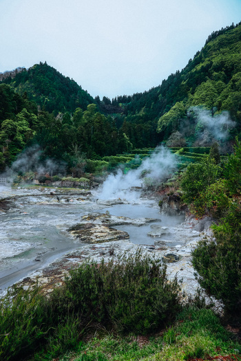 View of misty steam rising from the geothermal hot springs surrounded by lush green vegetation and mountains Furnas Azores Portugal.