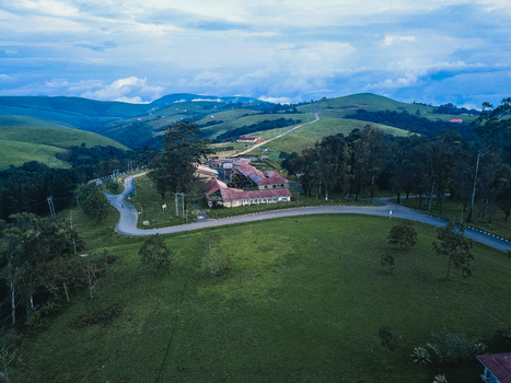 Aerial view of lush green hills a winding road and buildings with red roofs under a dramatic cloud filled sky Obudu Cross River Nigeria.