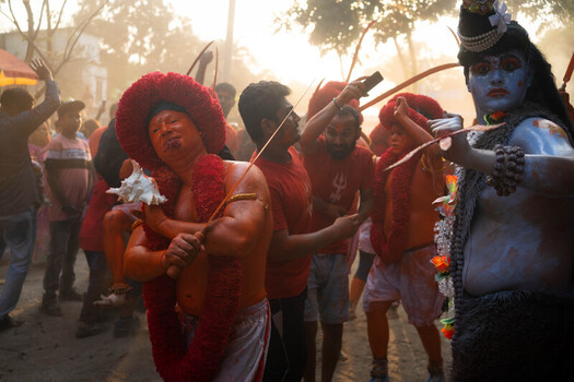Munshiganj Bangladesh 13 April 2025 View of vibrant procession with figures in vivid orange and blue body paint adorned with elaborate red headwear moving through a hazy golden light. Munshiganj Bangladesh 13 April 2025 View of vibrant procession with figures in vivid orange and blue body paint adorned with elaborate red headwear moving through a hazy golden light.