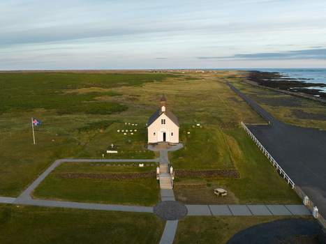 Aerial view of a serene white church standing gracefully amidst the vast green plains under a pastel sky Iceland Sveitarf&eacute;lagi&eth; &Ouml;lfus Iceland.