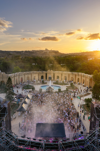 Aerial view of Park Nazzjonali Ta Qali during a music festival with a large crowd gathered in the amphitheater at sunset featuring a distant skyline in Attard Northern Region Malta. Aerial view of Park Nazzjonali Ta Qali during a music festival with a large crowd gathered in the amphitheater at sunset featuring a distant skyline in Attard Northern Region Malta.