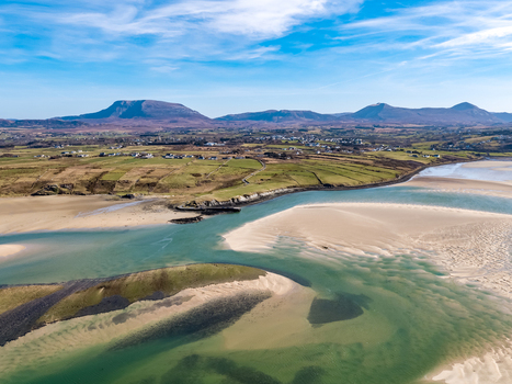 Aerial view of Ballyness Bay featuring expansive sandy tidal flats lush green coastal fields and distant mountains under a clear blue sky in Ballyness County Donegal Ireland. Aerial view of Ballyness Bay featuring expansive sandy tidal flats lush green coastal fields and distant mountains under a clear blue sky in Ballyness County Donegal Ireland.