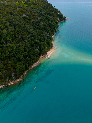 Aerial view of the coastline s lush forest meeting the turquoise sea with a lone kayak gliding through the tranquil waters Abel Tasman National Park Tasman Region New Zealand. Aerial view of the coastline s lush forest meeting the turquoise sea with a lone kayak gliding through the tranquil waters Abel Tasman National Park Tasman Region New Zealand.