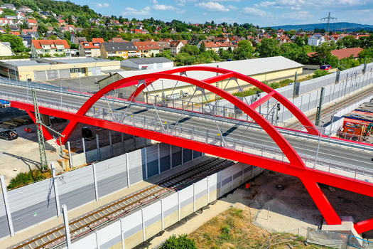 Aerial view of the red Piastenbrucke arch bridge crossing over railway tracks with residential houses and green hills in Forchheim Bayern Germany.