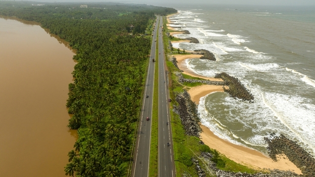 Aerial view of Maravanthe beach featuring a scenic highway running between the Arabian Sea and the Suparnika River with lush palm trees and sandy coastline in Maravanthe Karnataka India. Aerial view of Maravanthe beach featuring a scenic highway running between the Arabian Sea and the Suparnika River with lush palm trees and sandy coastline in Maravanthe Karnataka India.