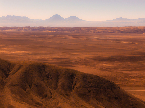 Aerial view of the arid landscape of the Atacama Desert with distant volcanic mountains under a clear sky in Antofagasta Chile.