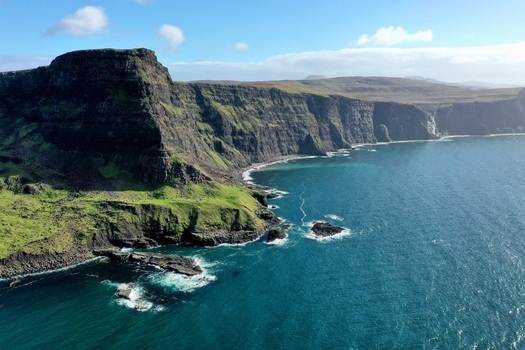 Aerial view of Waterstein Head featuring dramatic sea cliffs lush green slopes and deep blue coastal waters in Isle of Skye Scotland United Kingdom. Aerial view of Waterstein Head featuring dramatic sea cliffs lush green slopes and deep blue coastal waters in Isle of Skye Scotland United Kingdom.