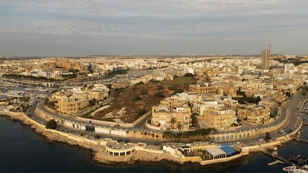 Aerial view of the coastal area featuring a marina with numerous boats historic limestone buildings and a winding waterfront road in Malta. Aerial view of the coastal area featuring a marina with numerous boats historic limestone buildings and a winding waterfront road in Malta.
