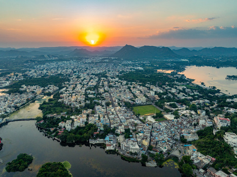 Aerial view of Udaipur city at sunset featuring the historic urban landscape surrounding lakes and distant hills under a golden sky in Udaipur Rajasthan India.