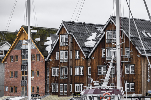 Tromso Norway 11 March 2026 View of traditional wooden waterfront buildings with snow on rooftops and sailboat masts in the harbor. Tromso Norway 11 March 2026 View of traditional wooden waterfront buildings with snow on rooftops and sailboat masts in the harbor.