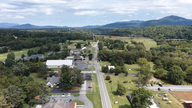 Aerial view of the rural landscape and road in Nellysford featuring green fields scattered buildings and distant mountains under a cloudy sky in Nellysford Virginia United States. Aerial view of the rural landscape and road in Nellysford featuring green fields scattered buildings and distant mountains under a cloudy sky in Nellysford Virginia United States.