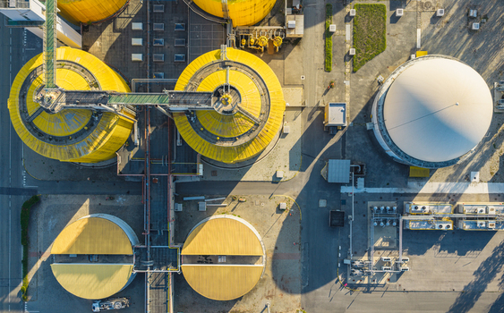 Aerial view of industrial anaerobic digestion tanks pipelines and biogas storage infrastructure at a wastewater treatment facility in Italy.