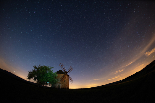 View of a historic stone windmill standing beside a tree under a vast starry night sky in the countryside of Brno City District South Moravian Region Czechia.