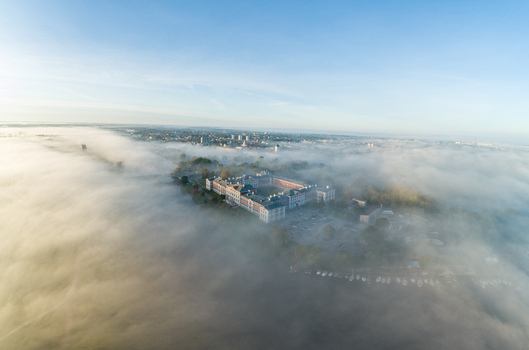 Aerial view of Jelgava Palace surrounded by thick morning fog with the surrounding city and river visible in the distance under a clear blue sky in Jelgava Latvia. Aerial view of Jelgava Palace surrounded by thick morning fog with the surrounding city and river visible in the distance under a clear blue sky in Jelgava Latvia.