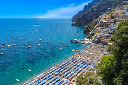 Aerial view of the colorful buildings of Positano clinging to the cliffs above a crowded beach with rows of umbrellas and boats in the turquoise sea Positano Campania Italy. Aerial view of the colorful buildings of Positano clinging to the cliffs above a crowded beach with rows of umbrellas and boats in the turquoise sea Positano Campania Italy.