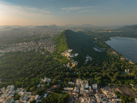 Aerial view of the historic Monsoon Palace perched atop a lush green hill overlooking the sprawling city of Udaipur and the serene waters of Fateh Sagar Lake in Udaipur Rajasthan India.