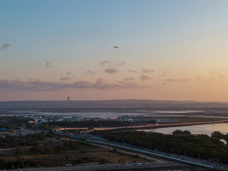 Aerial view of Bali Mandara Toll Road stretching across the coastal waters with mangroves and a distant airplane in the golden hour light in Kecamatan Kuta Selatan Bali Indonesia.
