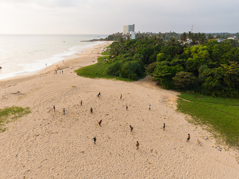 Aerial view of people playing cricket on a sandy beach along the tropical coastline with palm trees and the ocean Galle Southern Province Sri Lanka.