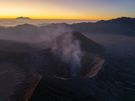 Aerial view of the smoking crater of Mount Bromo at sunrise with volcanic ridges and a golden sky in the background in Tosari East Java Indonesia.