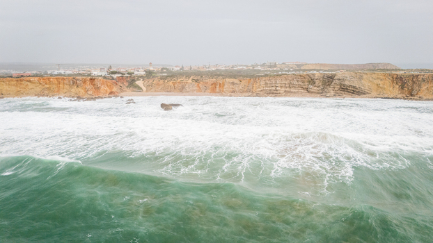 Aerial view of the rugged coastline of Sagres with turquoise waves crashing against steep cliffs under an overcast sky in Sagres Faro Portugal. Aerial view of the rugged coastline of Sagres with turquoise waves crashing against steep cliffs under an overcast sky in Sagres Faro Portugal.