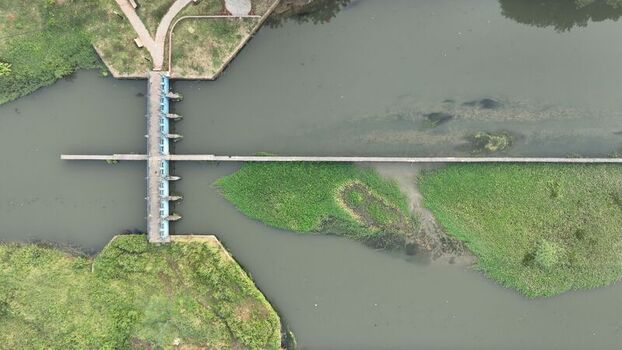 Aerial view of a concrete dam structure spanning a river with lush green vegetation and water flowing through the sluice gates in Bekasi Barat West Java Indonesia. Aerial view of a concrete dam structure spanning a river with lush green vegetation and water flowing through the sluice gates in Bekasi Barat West Java Indonesia.