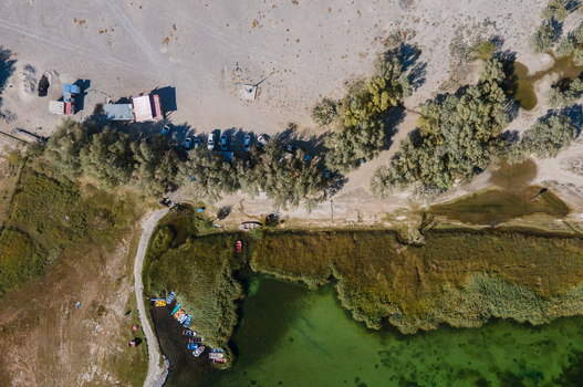 Aerial view of Blind Lake Sarfaranga Shigar with small boats docked along the green shoreline surrounded by trees and a sandy parking area in Skardu Gilgit Pakistan.
