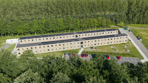Aerial view of a long modular residential building surrounded by lush green trees and a parking lot in Middenmeer North Holland Netherlands.