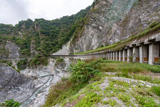 View of the concrete tunnel structure along the steep rocky cliffs of Taroko National Park with a river flowing below in Xiulin Township Hualien County Taiwan.