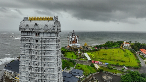 Aerial view of the Murudeshwar Temple complex featuring the towering Raja Gopura and the massive Shiva statue overlooking the Arabian Sea under a cloudy sky in Murdeshwar Karnataka India.